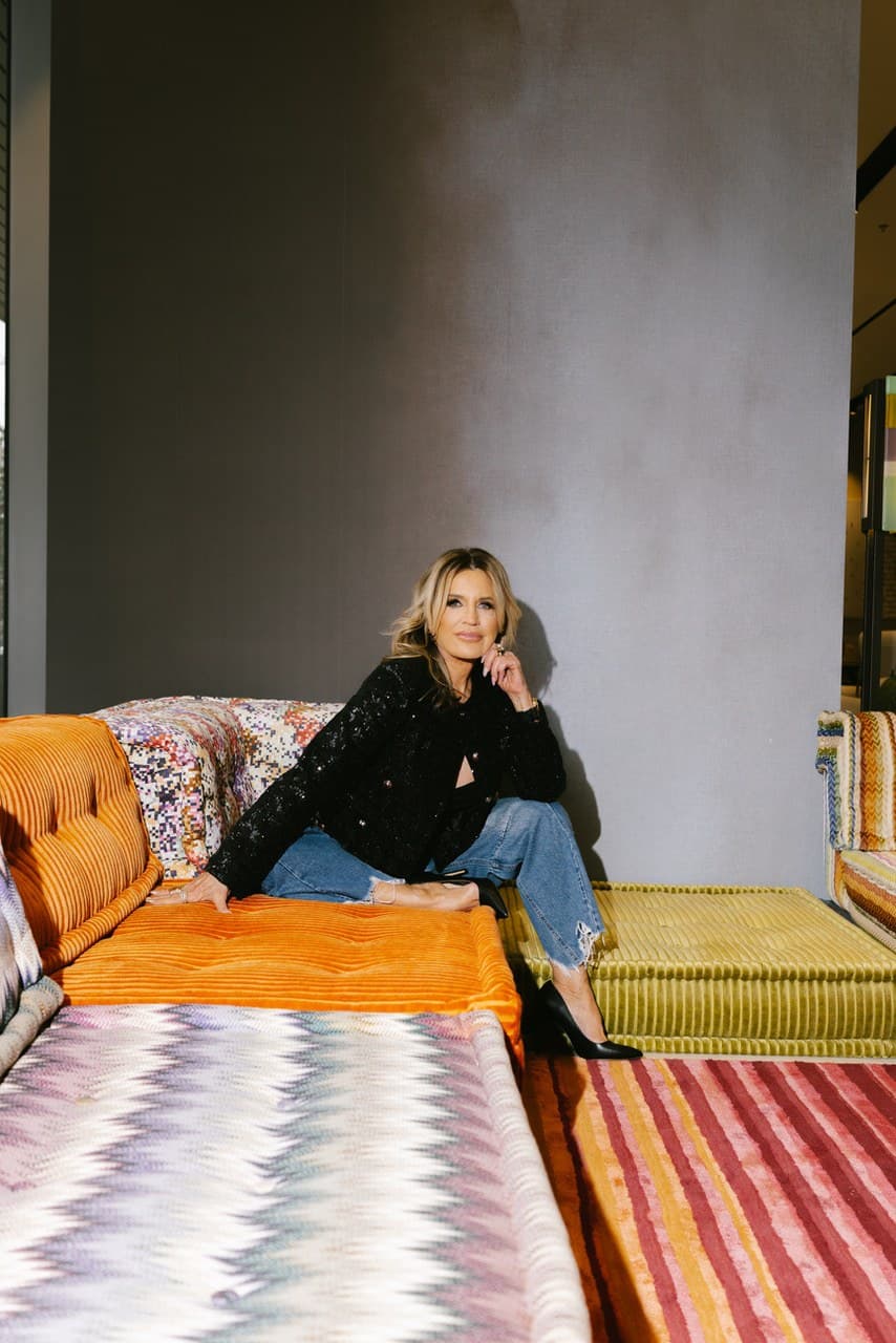 Giselle Koy in a black sequin jacket, seated in the corner of a colorful Mah Jong modular sofa